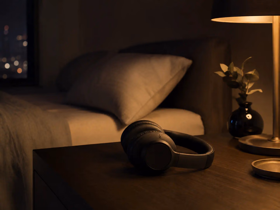 Headphones resting on a nightstand beside a warm bedside lamp
